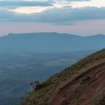 Paisagem montanhosa de Minas Gerais com encosta gramada e nuvens carregadas ao entardecer