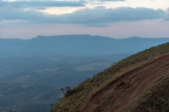 Paisagem montanhosa de Minas Gerais com encosta gramada e nuvens carregadas ao entardecer