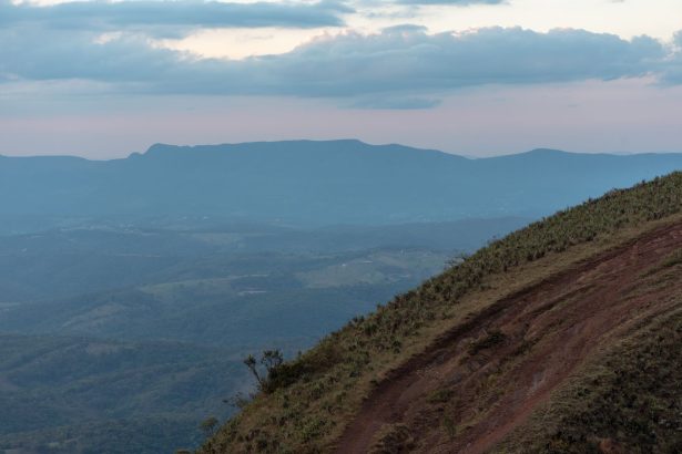 Paisagem montanhosa de Minas Gerais com encosta gramada e nuvens carregadas ao entardecer