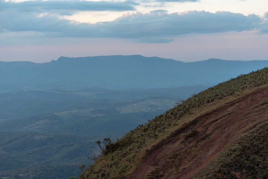 Paisagem montanhosa de Minas Gerais com encosta gramada e nuvens carregadas ao entardecer