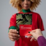 Mãos trocam um folheto sobre voluntariado e conscientização ambiental.