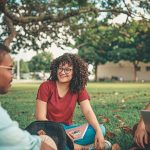 Grupo de estudantes conversa e realiza atividades em uma área externa de um campus universitário.