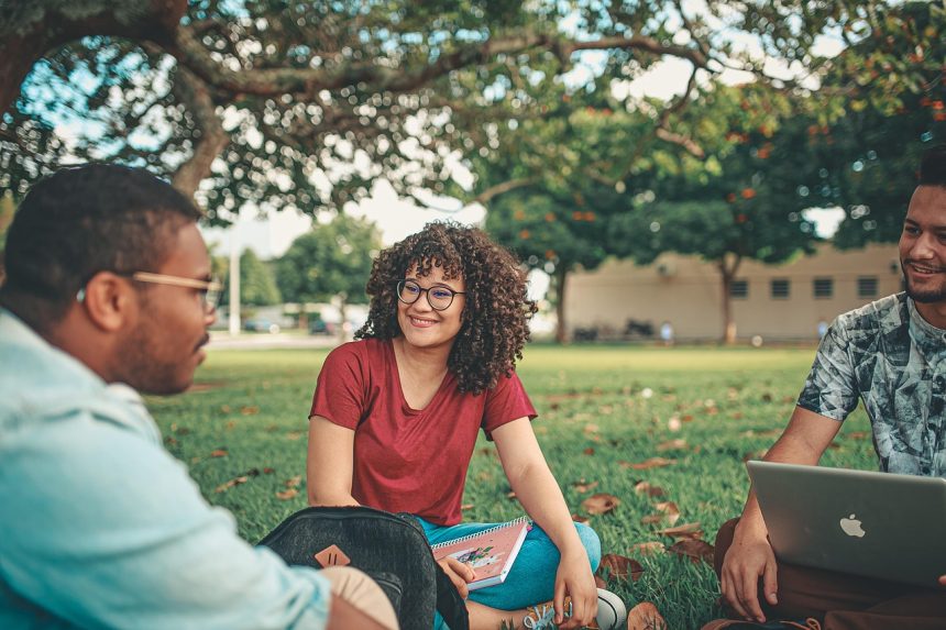 Grupo de estudantes conversa e realiza atividades em uma área externa de um campus universitário.